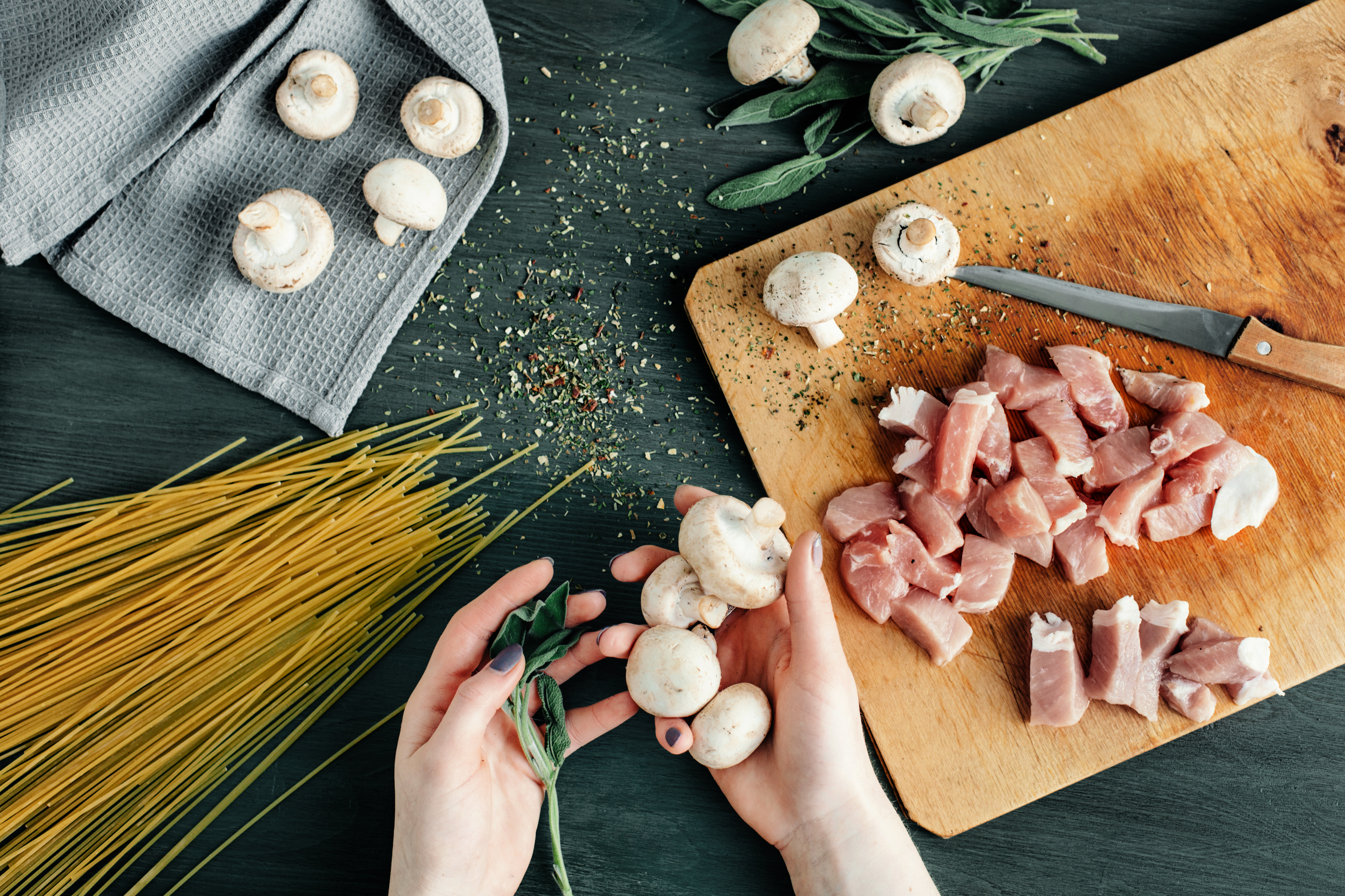 Henkilön kädet käsittelemässä lihaa ja sieniä ruoanlaiton yhteydessä.