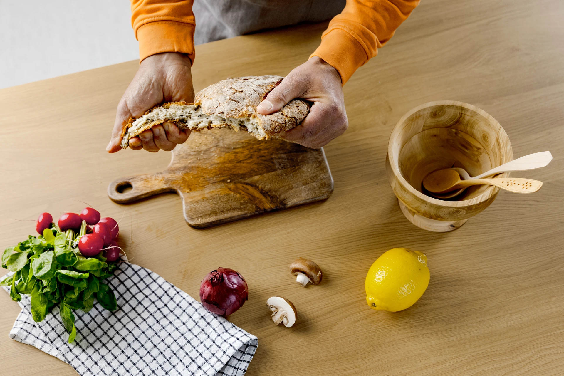 Henkilö repii käsillä kauraleivästä palaa keittiössä.