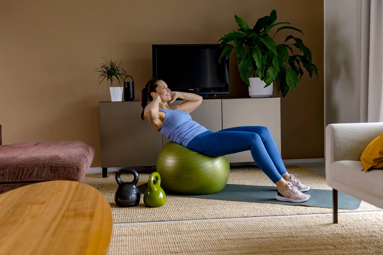 Nainen tekee vatsalihasliikettä jumppapallon päällä olohuoneessa.