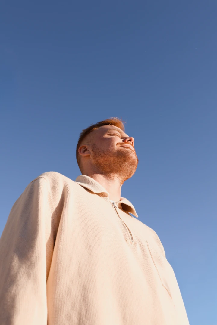 Auringonvalosta nauttiva mies kuvattuna alaviistosta sininen taivas taustalla.