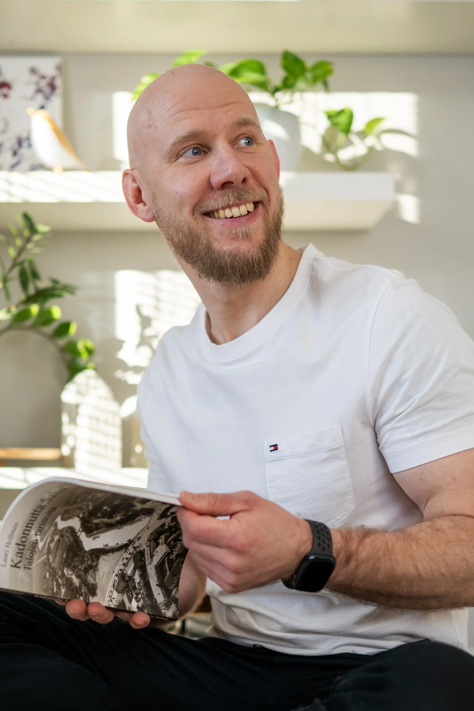 Kalju, parrakas mies hymyilee katsoen olkansa yli käsissään aikakausilehti.